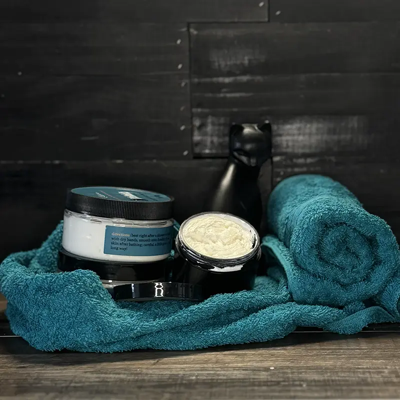 an artistically arranged product photo of lotion bottles with a towel and a little cup of lotion displayed