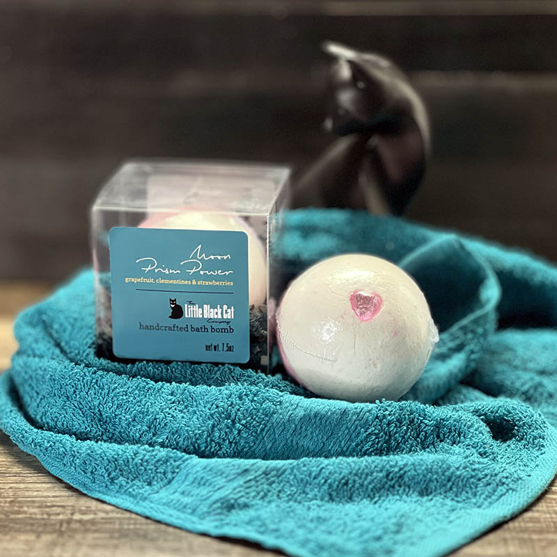 artistic arrangement of one boxed and one loose bath bomb with a towel and an art deco cat statue