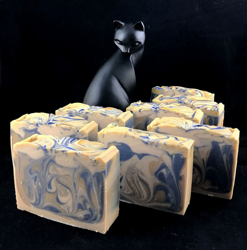 8 naked bars of gold, blue and tan soaps arranged  standing upright with an elegant cat statue presiding in the background