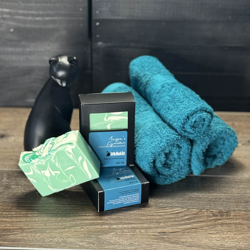 loyalty soap bars, one in box one out, nested in a basket of teal towels with a sassy cat looking up at the viewer